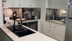 A modern kitchen with white cabinetry, a black sink, and a countertop with a sign reading "TREE TOPS." - TreeTops - wood fire, outdoor spa and great coffee (Hepburn Springs)