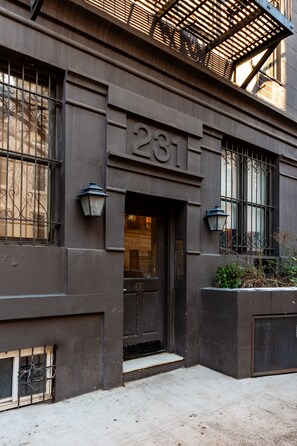 A building facade with a dark-colored entrance, a visible door number '281', and a small window with a metal grille. - Chelsea Living | Pet-Friendly | Marble Style (New York)