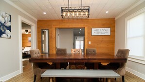 A dining area with a wooden table and chairs, a bench, a chandelier, and a sign on the wall.