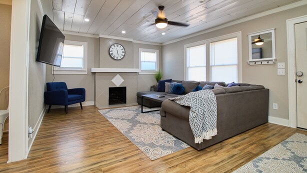 A living room with a gray sofa, blue armchair, and a flat-screen TV mounted on the wall.