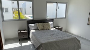 Quarto com uma cama, duas mesas de cabeceira, uma janela e vista para edifícios.