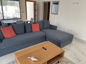 A modern living room with a grey sectional sofa, a wooden coffee table, and a dining area in the background.