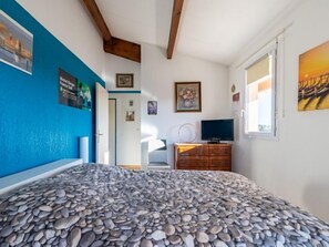 Een slaapkamer met een bed voorzien van een vloerpatroon van kleine steentjes, een houten dressoir, een televisie en diverse wanddecoraties.