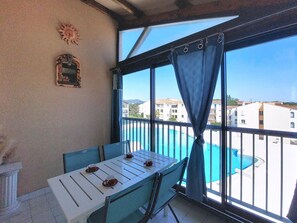 Ein Balkon mit Tisch und Stühlen, Blick auf einen Swimmingpool und Gebäude im Hintergrund.