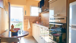 A compact kitchen with a dining area, a window, and a view of greenery outside. - Le Lagon Bleu by Interhome (Fréjus)