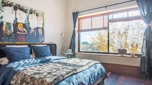 A bedroom with a large bed, a window with blinds, a painting on the wall, and a small table with a lamp. - Le Mas Provençal by Interhome (Jonquieres Saint Vincent)