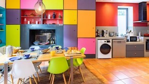 A modern kitchen with colorful cabinets, a dining area with a table and chairs, and a built-in washing machine. - Le Mas Provençal by Interhome (Jonquieres Saint Vincent)