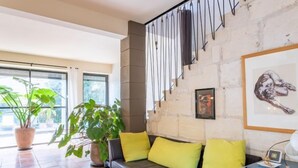 A modern living room with a leather sofa, yellow cushions, potted plants, and artwork on the walls. - Le Mas Provençal by Interhome (Jonquieres Saint Vincent)