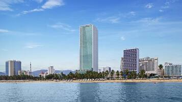 A coastal cityscape with high-rise buildings, a beach, and clear skies.