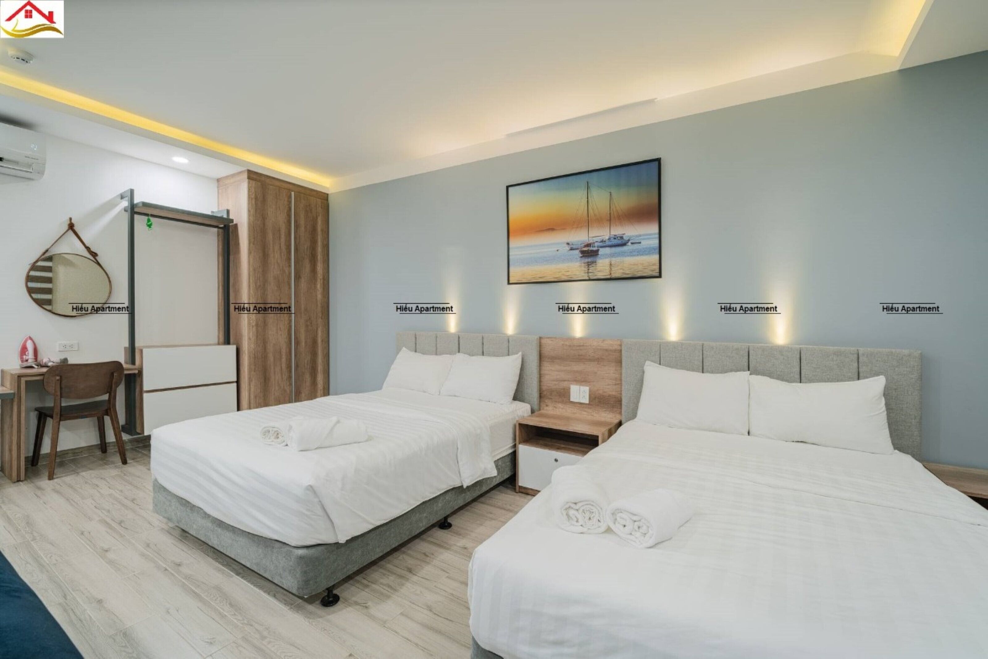 Quarto de hotel com duas camas, uma escrivaninha, uma cadeira, um espelho e um quadro na parede.