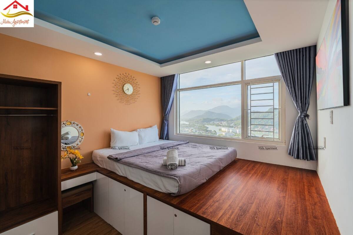 A bedroom with a bed, a desk, a window with a view, and a ceiling with a blue accent.