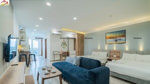 A modern hotel room with a large bed, a blue sofa, a small table with cups, a TV, and a desk with a chair. - Tony Luxury Apartment - Venue Stay (Nha Trang)