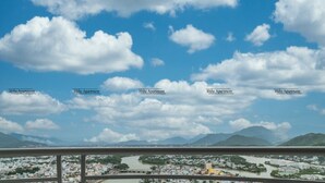 A balcony with two white plastic chairs, a table with a teapot, and a view of a cityscape with a river and mountains in the distance. - Tony Luxury Apartment - Venue Stay (Nha Trang)