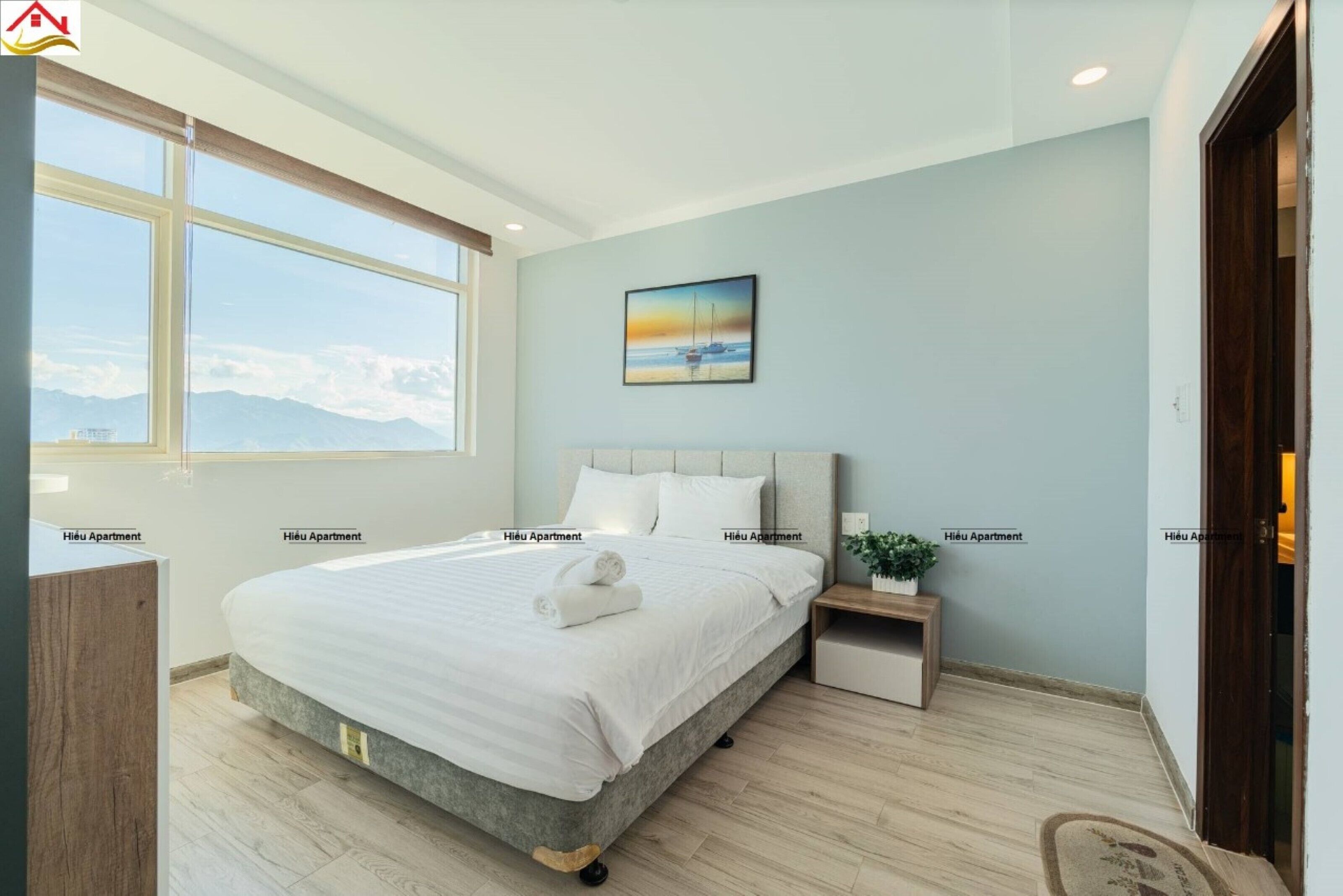 Un dormitorio con una cama grande, una mesita de noche, una ventana con vistas a las montañas y un cuadro en la pared.