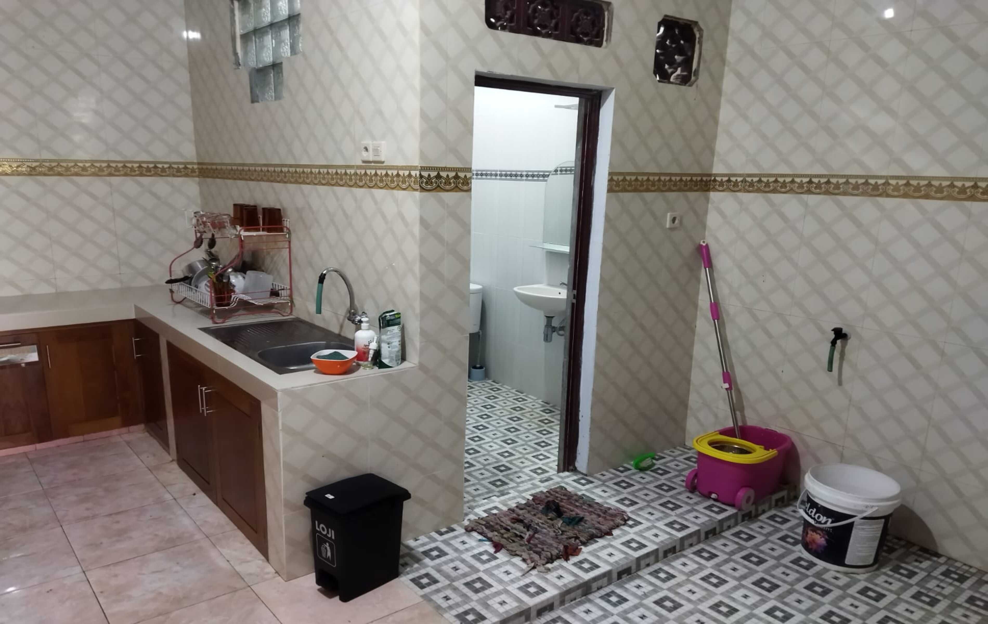 A kitchen with a sink, cabinets, and a dish rack. There is a door leading to a bathroom with a sink and toilet.