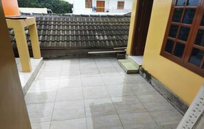 A tiled courtyard with a tiled roof, a wooden table, and a yellow wall with a window. - Algira Homestay Prambanan (Prambanan)