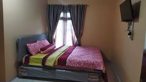 A single bed with a mattress cover, a headboard, and pillows. There is a window with curtains, a wall-mounted TV, and a power outlet on the wall. - Algira Homestay Prambanan (Prambanan)