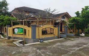 A house with a yellow exterior, a gated entrance, and a signboard. - Algira Homestay Prambanan (Prambanan)