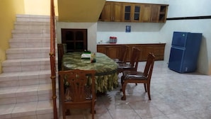 A dining area with a round table, chairs, a staircase, wooden cabinets, and a blue refrigerator. - Algira Homestay Prambanan (Prambanan)