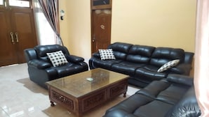 A living room with two black leather sofas, a wooden coffee table, and a checkered pillow on each sofa. - Algira Homestay Prambanan (Prambanan)