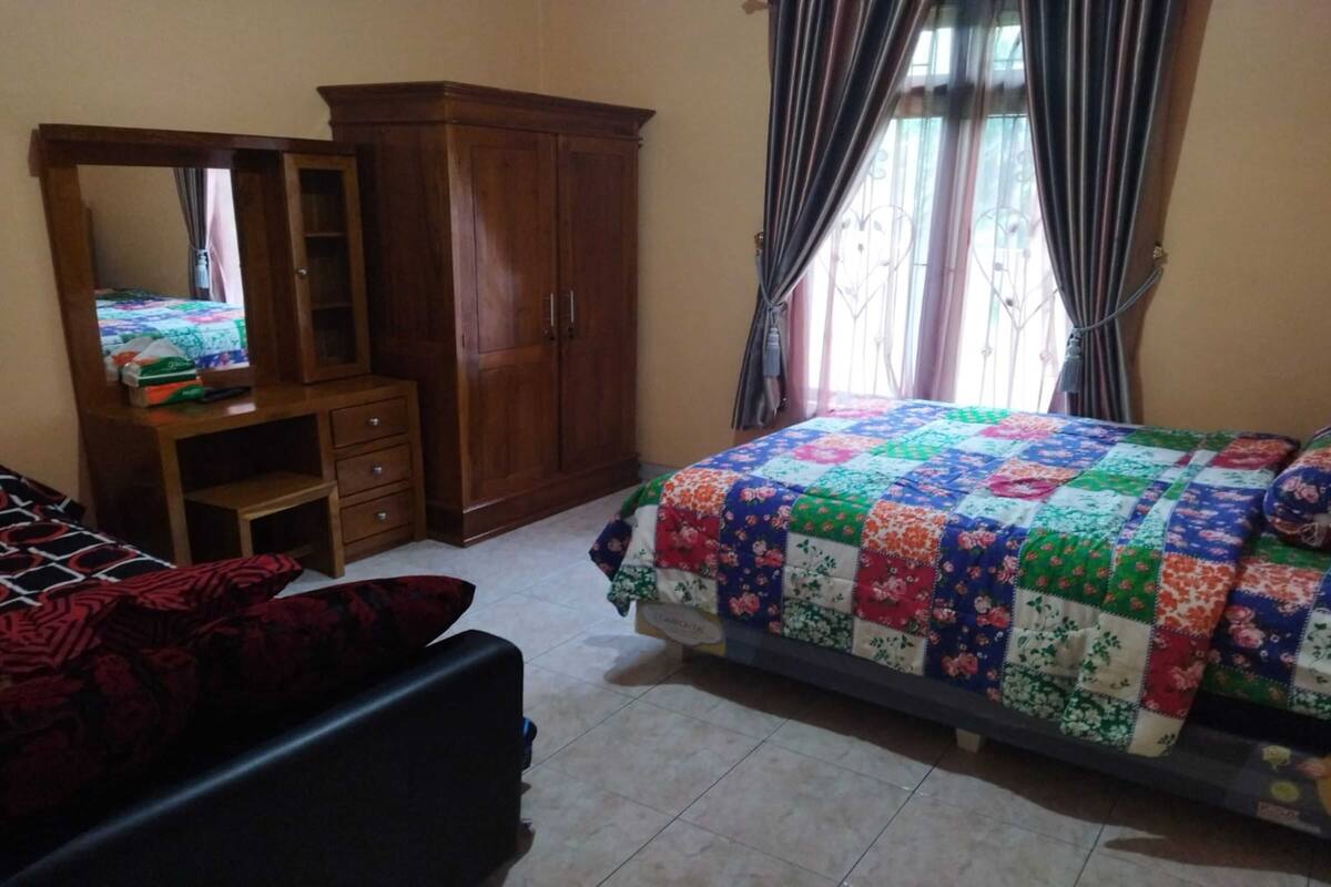 Une chambre à coucher avec un lit, une armoire en bois, un petit bureau avec des tiroirs et un miroir.