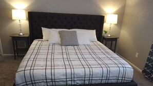 Een bed met een zwart hoofdeinde, zwart-wit geruit beddengoed, twee nachtkastjes met lampen, en een kleine plant op één nachtkastje.