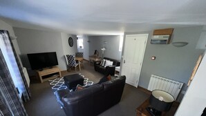 A living room with a black leather sofa, a television, a small table, and a chair. - Stylish Historic Apartment - Sleeps 3 & Parking (Norwich)