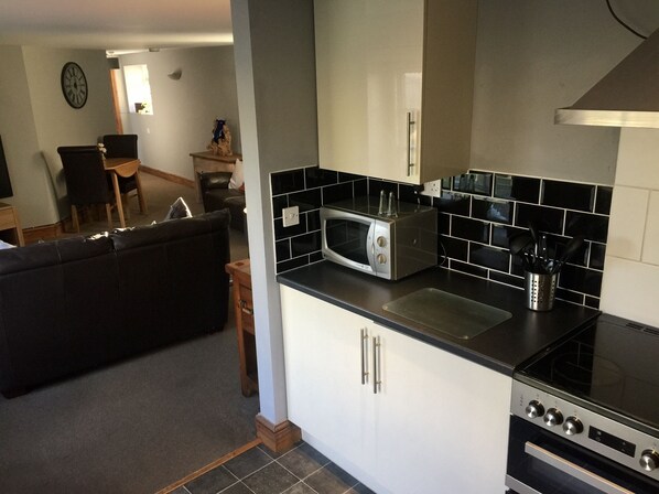 A compact kitchen with a microwave, toaster, and stove. There is a dining area with a chair and table visible in the background.