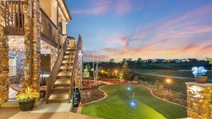 A stone staircase leading to a second floor, a well-lit outdoor area with a putting green, and a view of a distant landscape. - Sunset Casa: Golf & Lake Views, Hot Tub, Fire Pit, Sleeps 16 (Aurora)