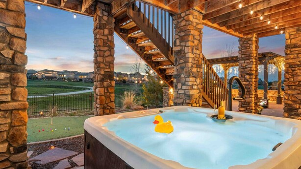 A hot tub with a duck float, stone pillars, and a view of a golf course. - Sunset Casa: Golf & Lake Views, Hot Tub, Fire Pit, Sleeps 16 (Aurora)