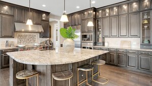 A modern kitchen with dark wood cabinets, a large island with stools, stainless steel appliances, and pendant lighting. - Sunset Casa: Golf & Lake Views, Hot Tub, Fire Pit, Sleeps 16 (Aurora)