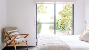 A bedroom with a bed, a chair, and a large window with a view of greenery. - The Villa | Margaret River (Margaret River)