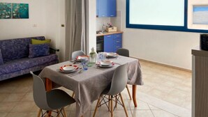Un comedor con una mesa preparada para cuatro personas, un sofá y una cocina al fondo.