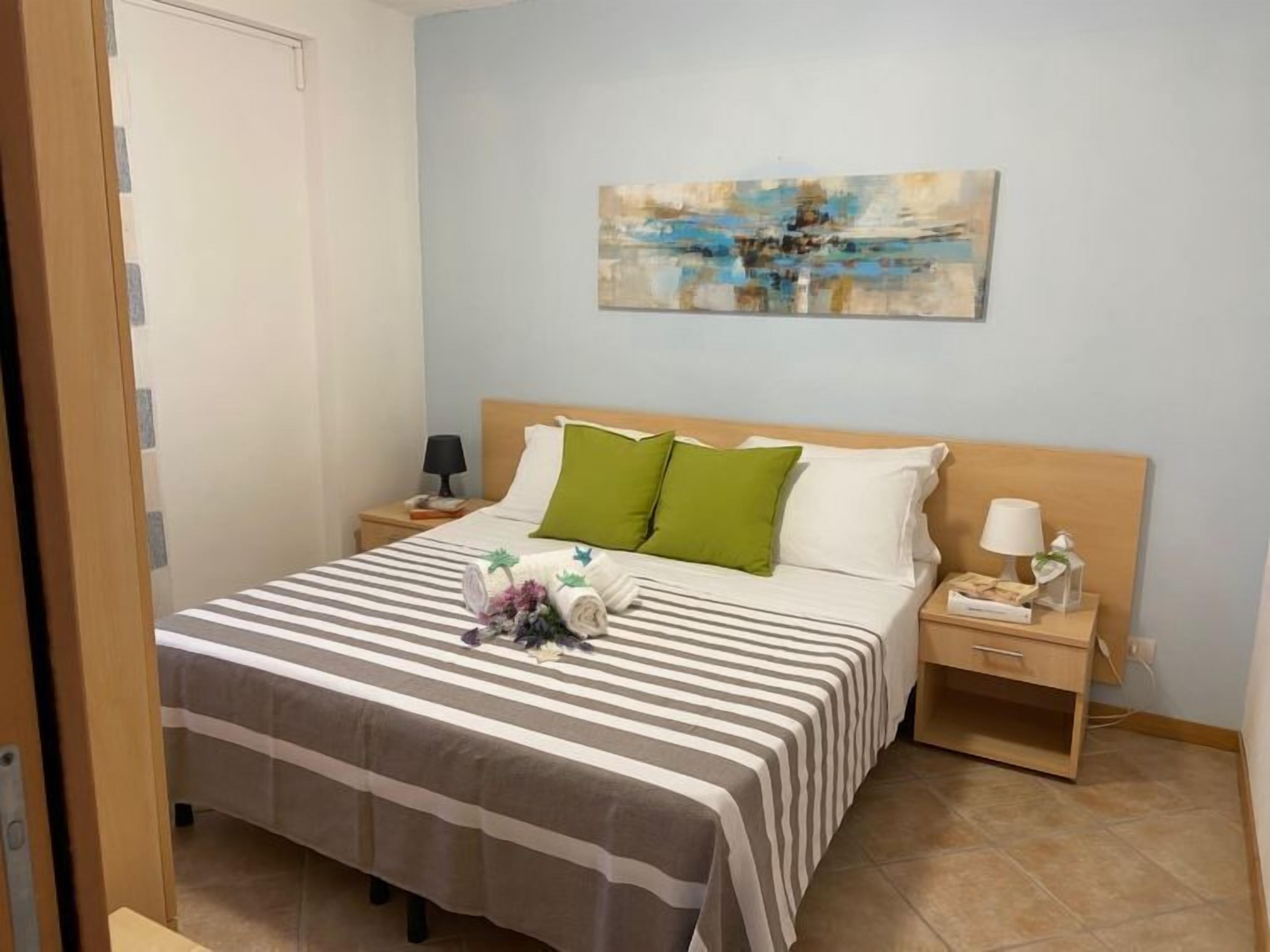 A neatly made bed with striped bedding, a wooden headboard, and a bedside table with a lamp and a small decorative item.