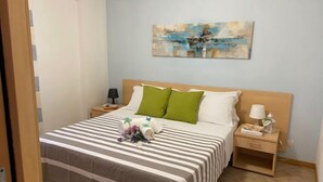 Una cama bien hecha con ropa de cama a rayas, cabecera de madera y mesita de noche con lámpara y un objeto decorativo pequeño.