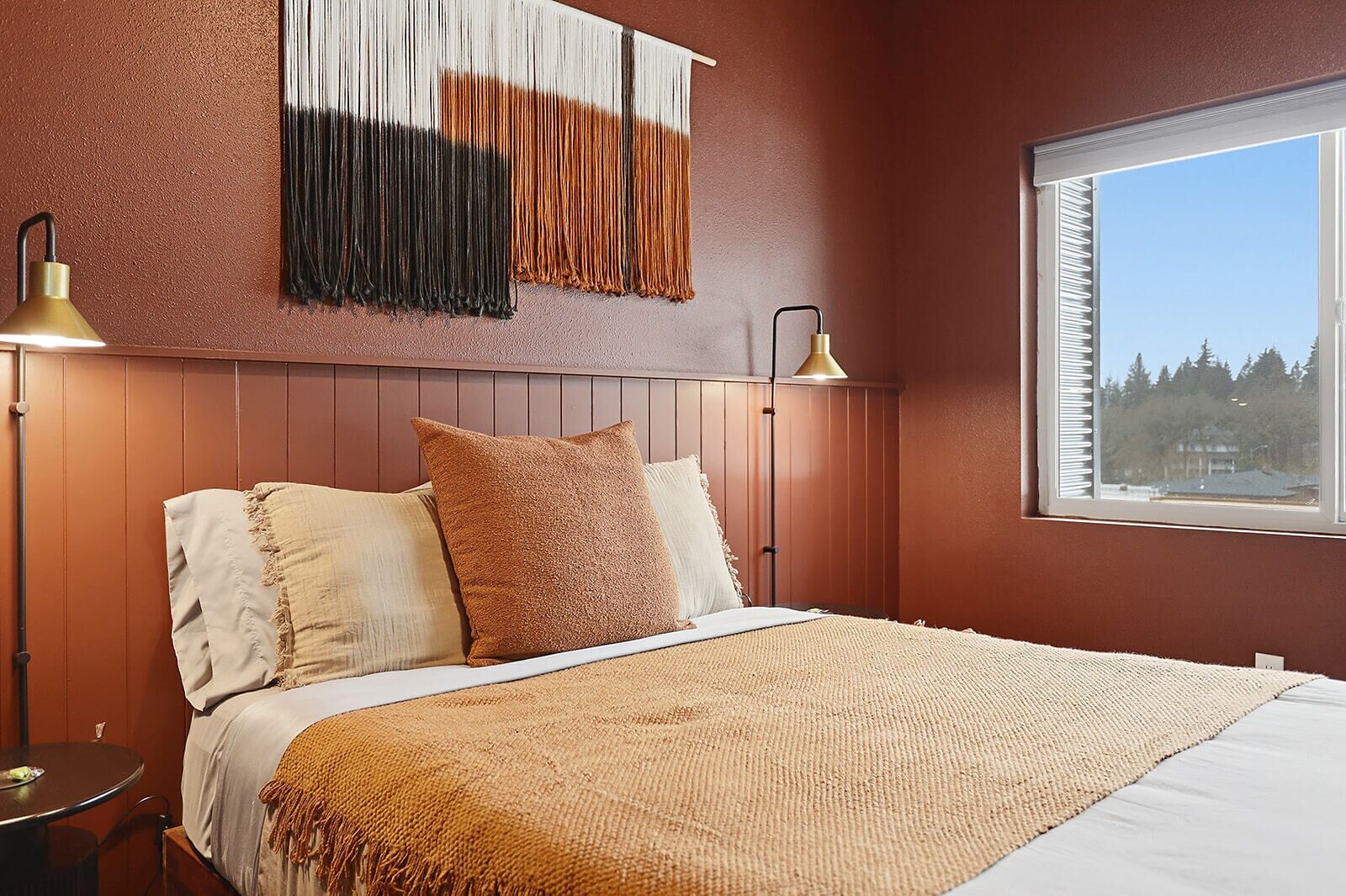 Ein Schlafzimmer mit Holz-Kopfteil, einem großen Fenster mit Blick und zwei Nachttischlampen.