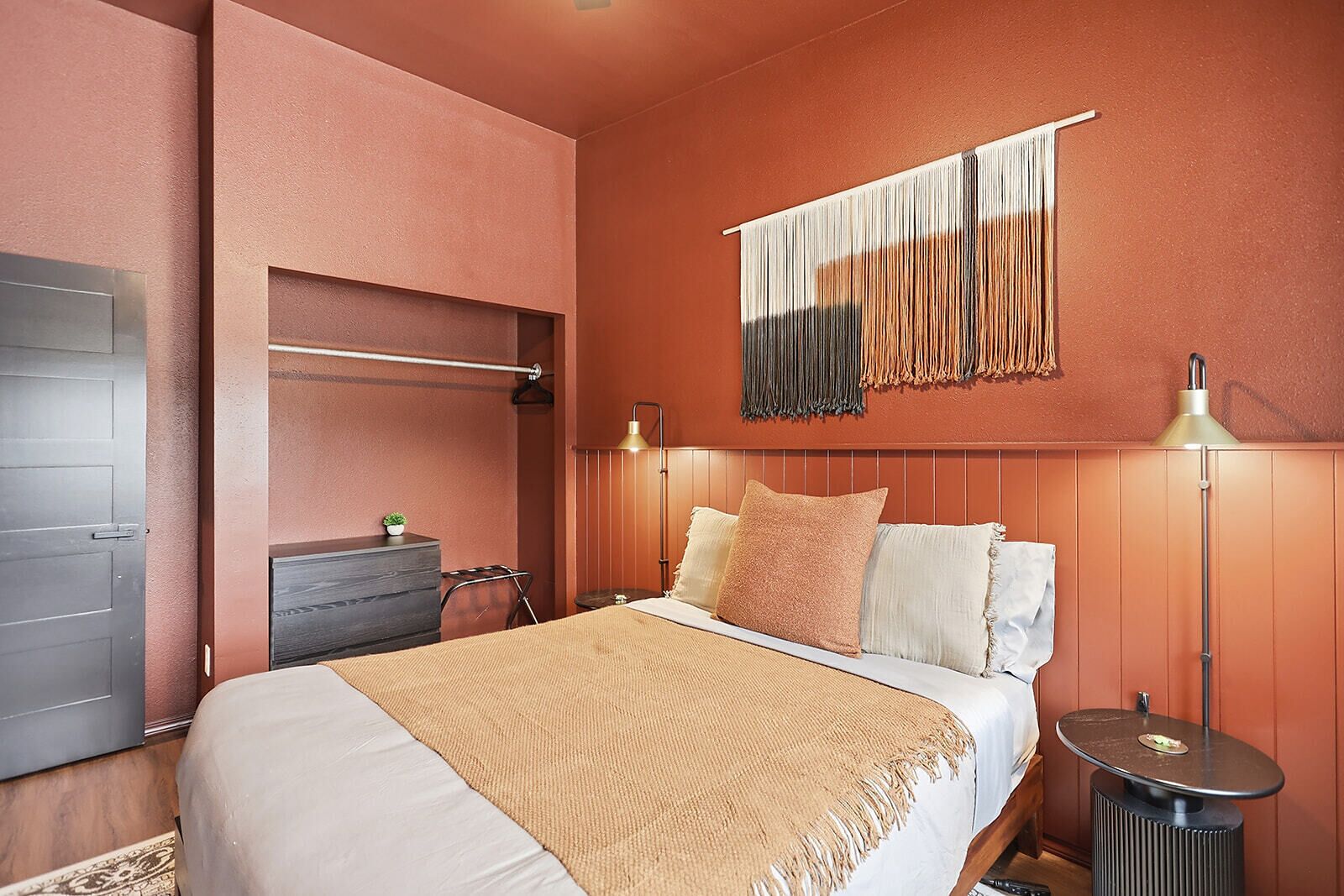A bedroom with a bed, bedside tables, a wall-mounted lamp, and a hanging macrame piece.