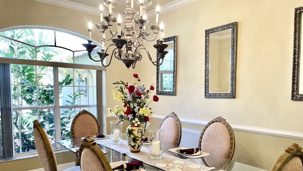 A dining room with a glass table, ornate chairs, a chandelier, and a vase of flowers. - Vacation Home In West Palm beach (WEST PALM BEACH)