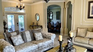 A living room with a patterned sofa, a coffee table with candles, and a chandelier. - Vacation Home In West Palm beach (WEST PALM BEACH)