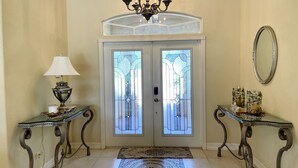 A foyer with a chandelier, two side tables with lamps, a large mirror, and a double door with stained glass. - Vacation Home In West Palm beach (WEST PALM BEACH)