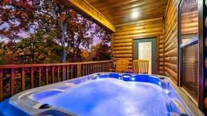 A wooden cabin with a hot tub on a balcony, surrounded by autumn trees.