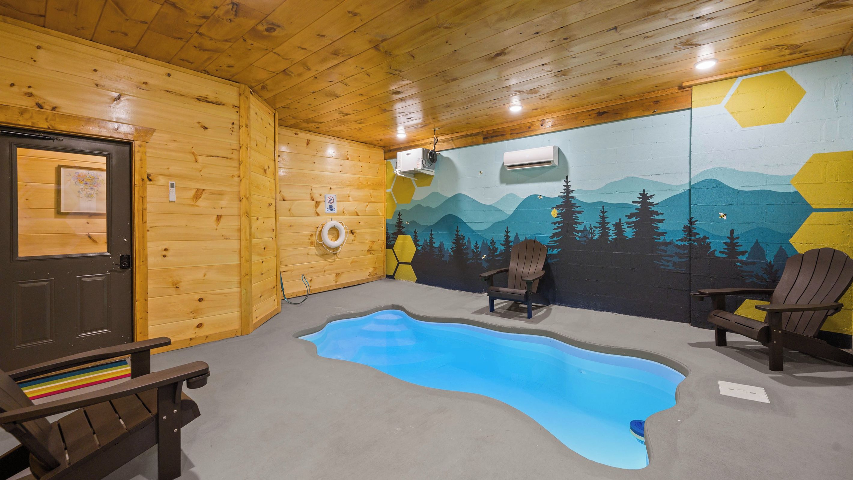 Una stanza con arredamento in legno, una piscina, due poltrone Adirondack e un murale raffigurante un paesaggio montano.