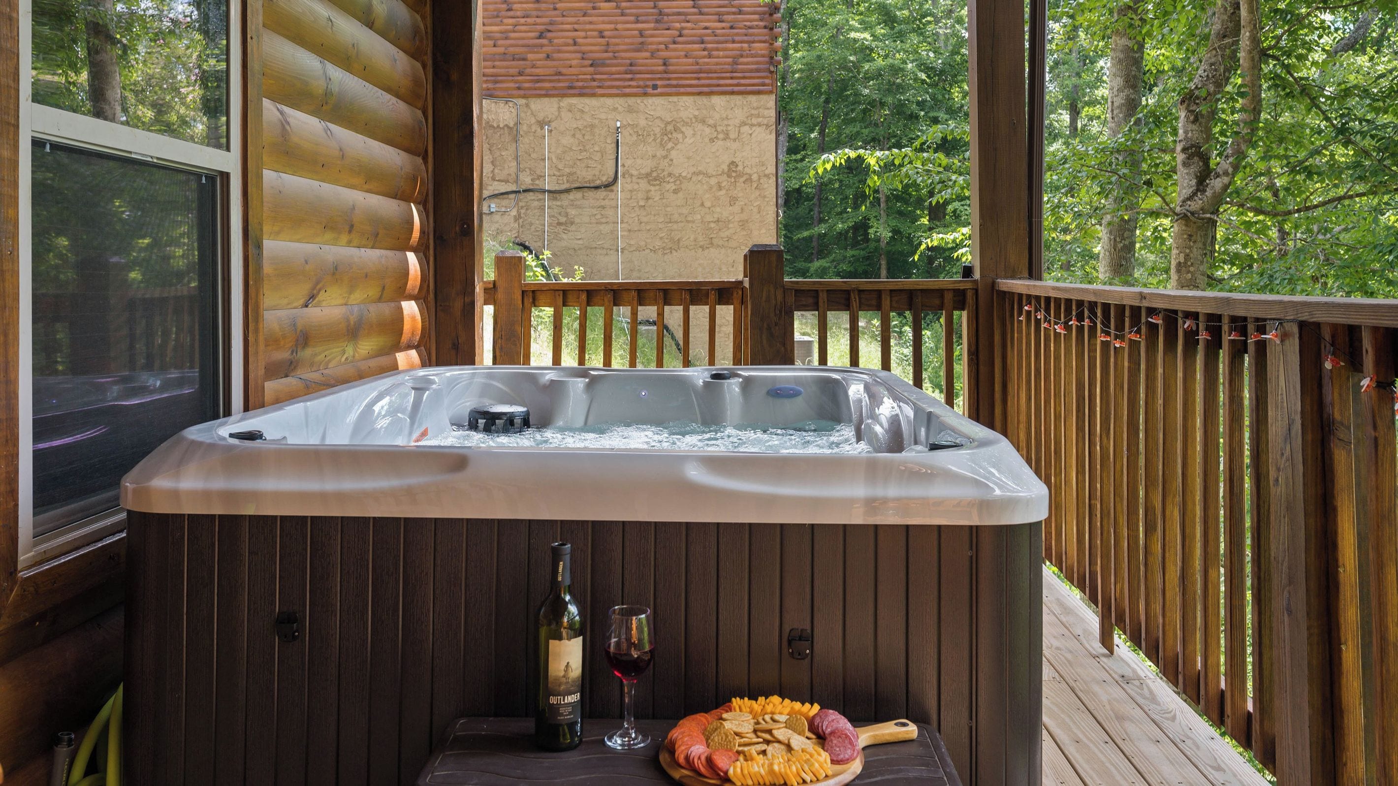 Een hottub op een houten terras met een houten omheining, een fles wijn en een vleeswarenplank.
