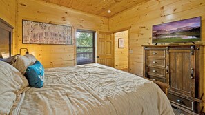 A wooden cabin bedroom with a bed, a dresser, a painting, and a television.