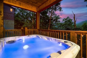 A hot tub on a wooden deck with a view of trees and a sunset. - Classic Log Cabin | Hot Tub, Pool, Games & Dogs OK (Sevierville)