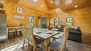 A wooden cabin interior with a dining area, kitchen, and living room.