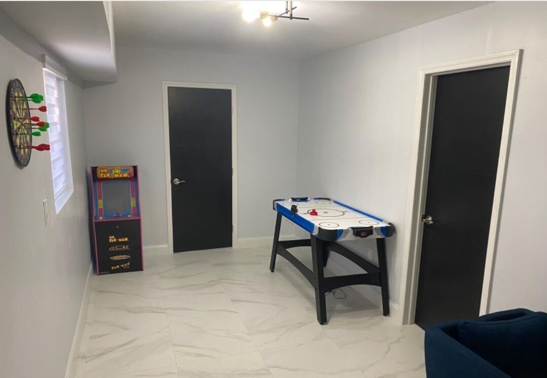 A room with a foosball table, a dartboard, and a Pac-Man arcade machine.