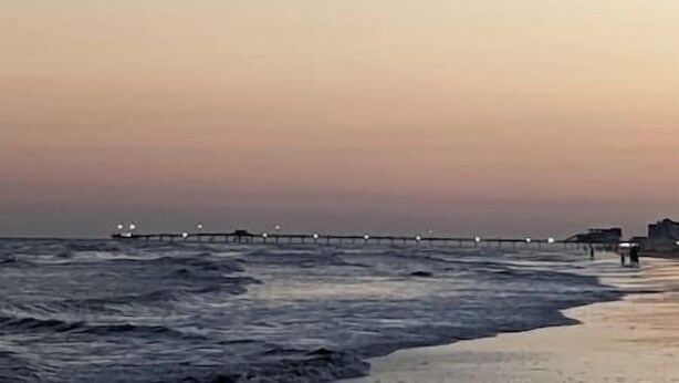 Une plage avec une jetée qui s’avance dans l’eau.