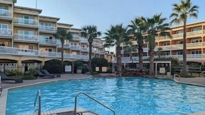 Une piscine entourée d’immeubles à plusieurs étages dotés de balcons, de palmiers et surplombant un ciel dégagé.
