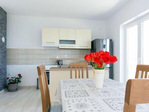 Uma cozinha moderna com armários em tons claros, uma geladeira de aço inoxidável e uma área de jantar com mesa posta para dois.